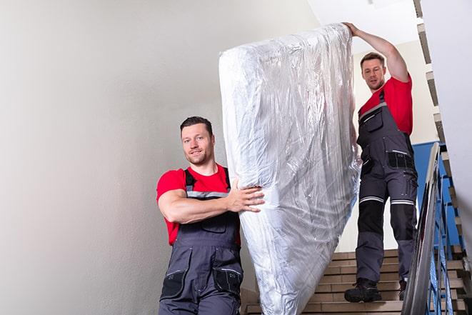 two workers hauling a box spring out of a building in Worden